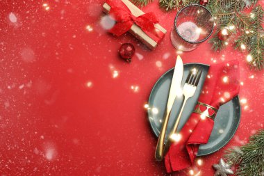 Tabaklı güzel bir Noel seti, şık çatal bıçak takımı ve kırmızı masa üzerinde şenlikli bir dekor. Mesaj için yer var. Bokeh etkisi