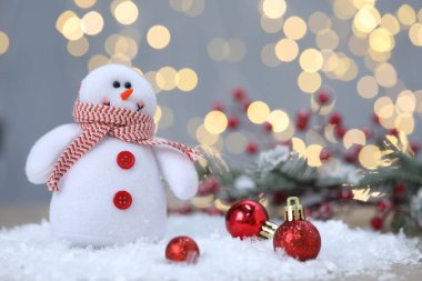 Komik kardan adam figürü ve bulanık ışıklara karşı yapay kar üzerinde Noel topları