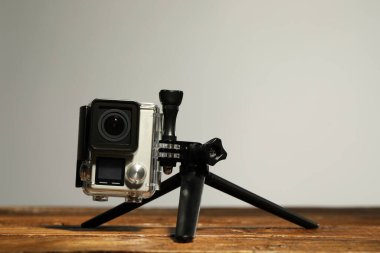 Gri arka planda, tahta yüzeyde modern aksiyon kamerası ve tripod. Metin için boşluk