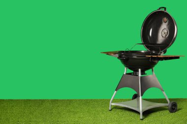 One black barbeque grill on grass against green background. Space for text clipart