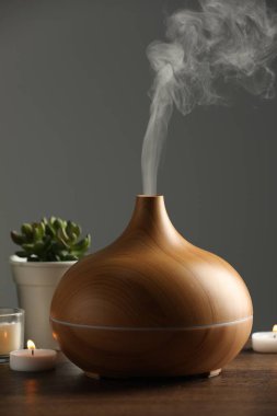 Aroma yağı yayıcı, ev bitkileri ve ahşap masada yanan mumlar.
