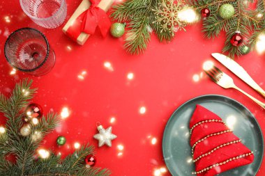 Tabaklı güzel bir Noel seti, şık çatal bıçak takımı ve kırmızı masa üzerinde şenlikli bir dekor. Mesaj için yer var. Bokeh etkisi