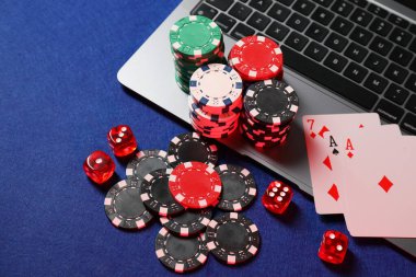 Poker fişleri, dizüstü bilgisayar, oyun kartları ve zarlar mavi masanın üstünde. Çevrimiçi oyun