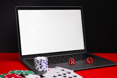 Laptop, poker fişleri, iskambil kağıtları ve zarlar kırmızı masada. Çevrimiçi oyun