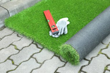 Gloves, level tool and roll of artificial turf outdoors