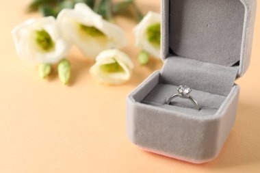 Kutusunda mücevher olan güzel bir yüzük ve bej arkaplanda çiçekler, yakın plan.