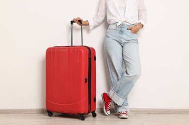 Kırmızı valizli kadın ışık duvarının yanında, yakın plan.