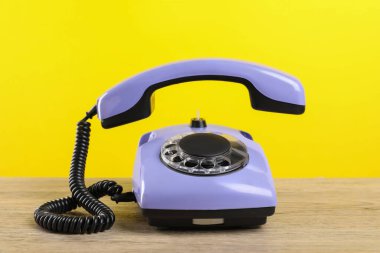 Sarı arka planda ahşap masanın üzerinde bir adet menekşe telefon.