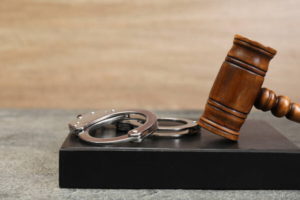 Книга, молоток судьи и наручники на сером текстурированном столе, крупный план. Пространство для текста