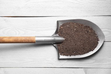 Açık gri ahşap masa üzerinde toprağı olan metal kürek, üst manzara.