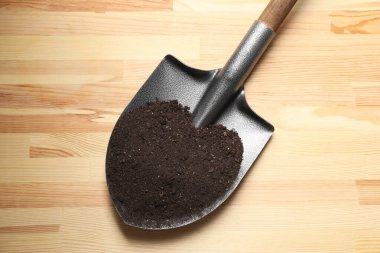 Hafif ahşap masa üzerinde toprağı olan metal kürek, üst görüş.