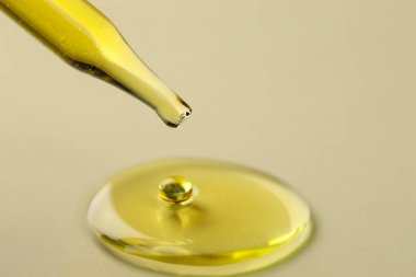 Koyu bej arka planda pipetten süzülen kozmetik yağı, yakın plan. Metin için boşluk