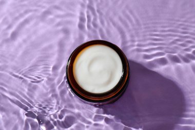 Menekşe arkaplanda su içinde yüz kremi olan kavanoz, üst görünüm