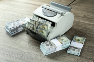 Tahta masanın üzerinde dolar banknotları olan para sayma makinesi.