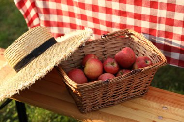 Bahçedeki ahşap bankta elma ve hasır şapkalı hasır sepet, yakın plan.