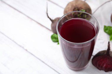 Bardakta taze pancar suyu ve açık ahşap masada olgun sebzeler, yakın plan. Metin için boşluk