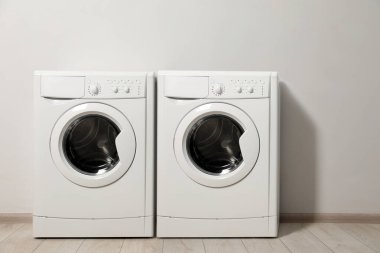 Açık gri duvarın yanında iki çamaşır makinesi