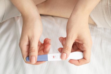 Woman holding positive pregnancy test indoors, closeup view clipart