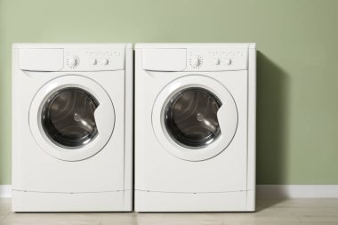 Açık yeşil duvarın yanında iki çamaşır makinesi