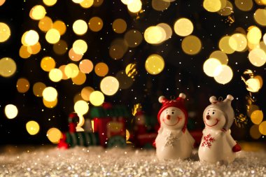 Siyah arka plana karşı sevimli kardan adam figürleri, bulanık Noel ışıkları, bokeh etkisi. Metin için boşluk