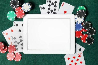 Poker fişleri, tablet ve iskambil kağıtları yeşil masada, düz yerde. Çevrimiçi oyun