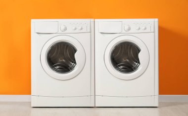 Turuncu duvarın yanında iki modern çamaşır makinesi