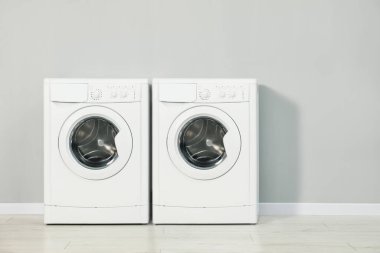Açık gri duvarın yanında iki çamaşır makinesi