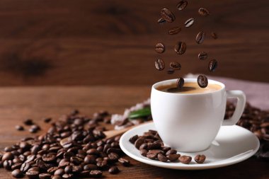 Kavrulmuş fasulye, ahşap masada aromatik kahve ile fincana düşüyor. Metin için boşluk