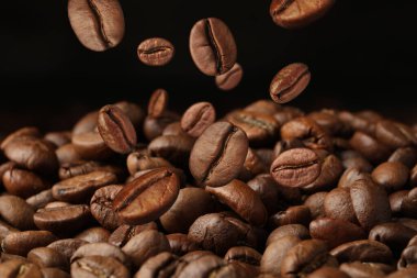 Kavrulmuş kahve çekirdekleri siyah arka plana doğru yığılıyor, yakın plan.