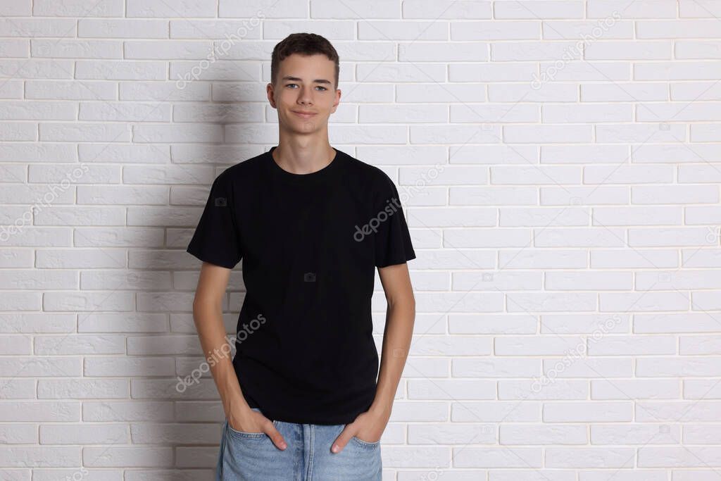 Teenage boy wearing black t-shirt near white brick wall, space for text