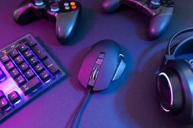 Bilgisayar faresi, kulaklık, RGB klavye ve oyun denetleyicileri koyu arkaplanda neon ışıkları, yakın plan