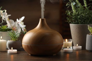 Aroma yağı yayıcı, yanan mumlar ve ahşap masa üzerinde bitkiler.
