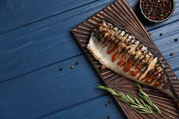 stock image Board with delicious grilled mackerel, peppercorns and rosemary on blue wooden table, flat lay. Space for text