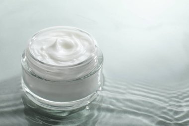 Açık yeşil arka planda su içinde yüz kremi olan kavanoz, yakın plan. Metin için boşluk