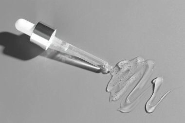 Gri arkaplandaki pipetten akan kozmetik serumu, üst görünüm