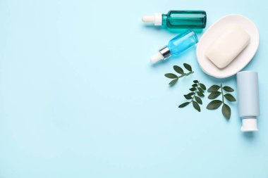 Farklı kozmetik ürünleri ve açık mavi arka planda yapraklar. Metin için boşluk