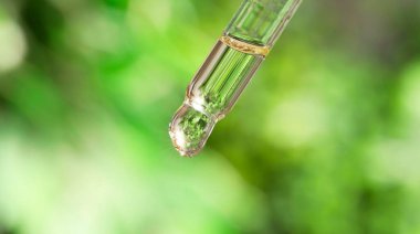 Pipetten damlayan temel yağ bulanık yeşil arka planda, yakın plan. Pankart tasarımı