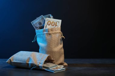 Gri masadaki çuval çuvallardaki dolar banknotları neon ışıklardaki koyu arkaplana karşı