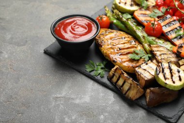 Gri masadaki sosla servis edilen lezzetli ızgara sebzeler ve tavuk göğsü, yakın plan. Metin için boşluk