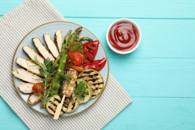 Lezzetli ızgara sebzeler ve açık mavi ahşap masada servis edilen soslu tavuk eti. Metin için boşluk