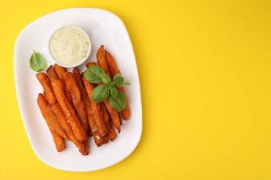 Tatlı patates kızartması, fesleğen ve soslu sarı arka plan, üst manzara. Metin için boşluk