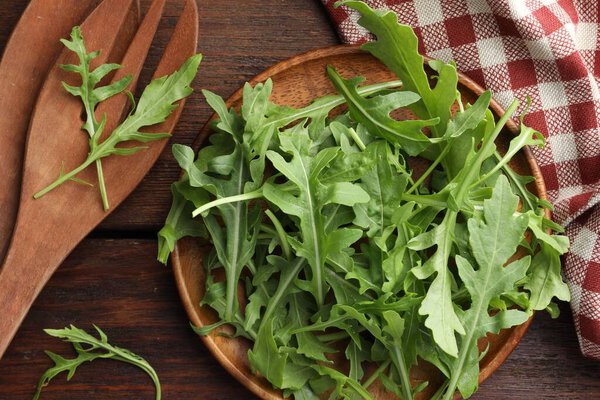 Fresh green arugula leaves and cutlery on wooden table, flat lay
