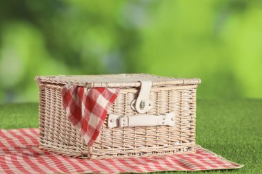 Bir piknik sepeti, kareli peçete ve çimlerin üzerindeki battaniye, bulanık yeşil arka plan, yakın plan.