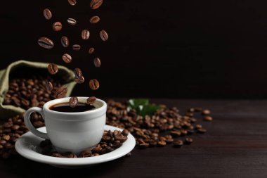 Kavrulmuş fasulye, ahşap masada aromatik kahve ile fincana düşüyor. Metin için boşluk