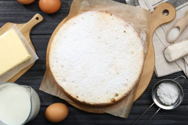 Lezzetli sünger keki ve siyah ahşap masa üzerindeki malzemeler.