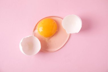 Kırık çiğ yumurta, pembe arka planda kabuk, üst manzara.