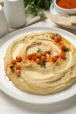 Zeytinyağlı lezzetli humus, beyaz ahşap masada nohut ve kırmızı biber, yakın plan.