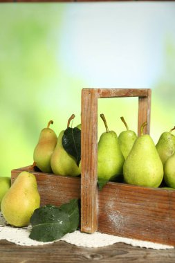 Taze armut ve yapraklı sandık ahşap masada bulanık yeşil arka planda, yakın plan.