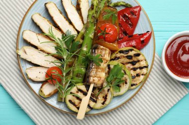 Lezzetli ızgara sebzeler ve açık mavi ahşap masada servis edilen soslu tavuk eti.