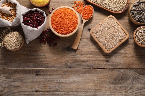 Different types of cereals, seeds and legumes on wooden table, flat lay. Space for text
